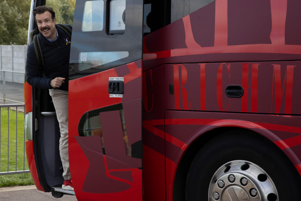 Photo from Ted Lasso, with Ted leaning out of the door of a red bus