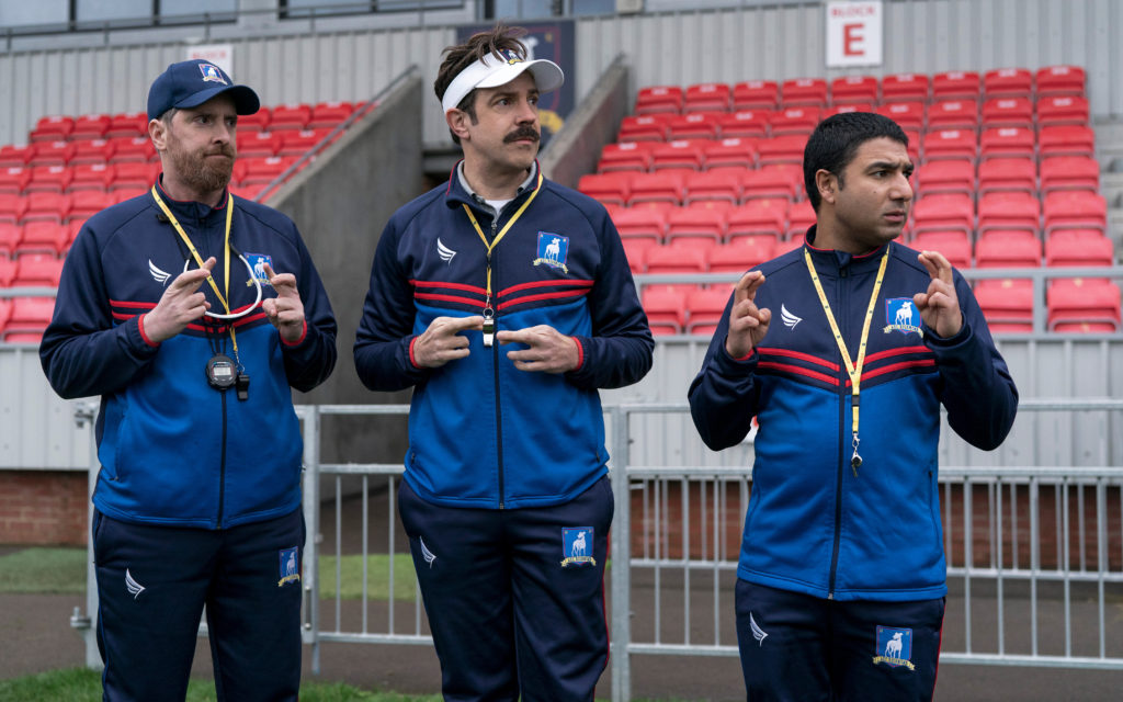 Photo from Ted Lasso, where Ted, Coach Beard, and Nate are crossing their fingers