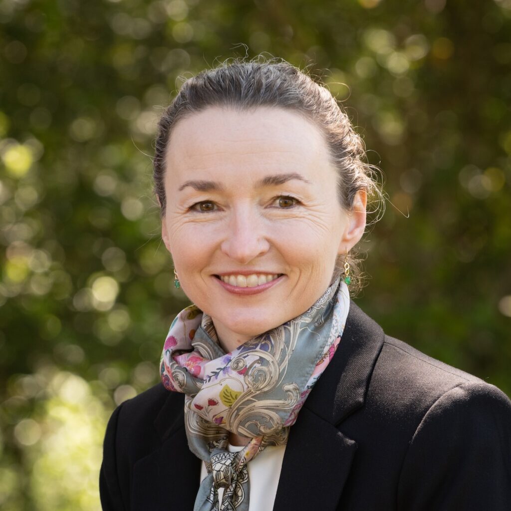 A headshot of Joanna Gardner smiling with a background of blurry green trees.